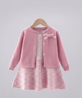 Pink checkered dress with a matching cardigan on a hanger against a clothing rack background.