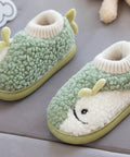 Children's green and white slippers with a face design held by a hand on a gray surface.