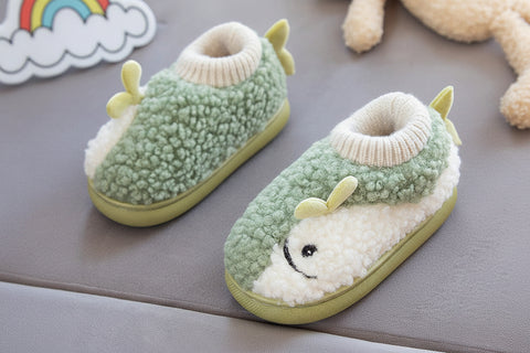 Children's green and white slippers with a face design held by a hand on a gray surface.