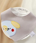 Baby bib with cartoon dog design and 'GALETTE' branding on a beige background