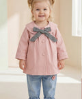 Child wearing a pink coat with a large bow, standing against a light background