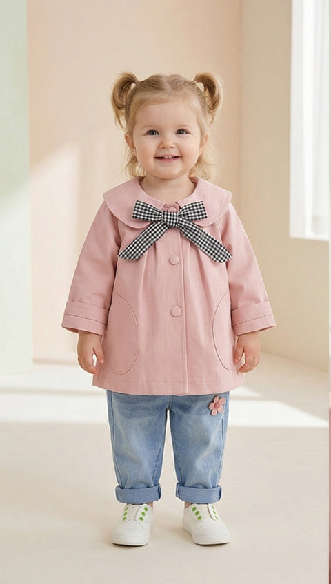 Child wearing a pink coat with a large bow, standing against a light background