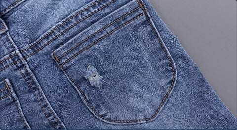 Close-up of a blue denim pocket with a small tear on a gray background