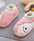 Pink and white baby booties with a smiley face held by a hand on a gray surface.