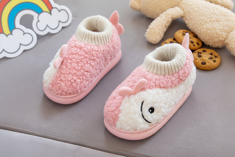 Pink and white baby booties with a smiley face held by a hand on a gray surface.
