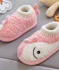 Pink and white baby booties with a smiley face held by a hand on a gray surface.