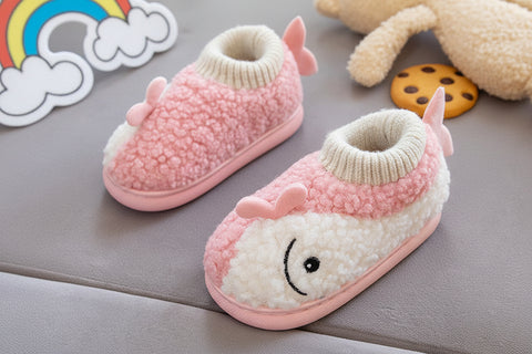 Pink and white baby booties with a smiley face held by a hand on a gray surface.