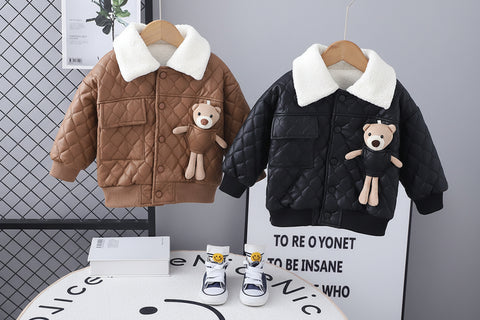Two children's quilted jackets on hangers with teddy bears attached, placed on a table with sneakers below.