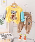 Children's outfit with yellow shirt, brown pants, and matching shoes on hangers against a white wall.