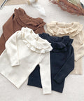 Four long-sleeve shirts in brown, white, beige, and navy with ruffled collars on a light surface.