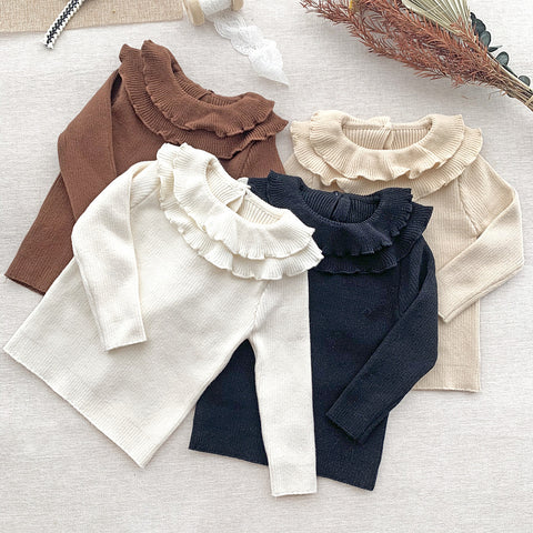 Four long-sleeve shirts in brown, white, beige, and navy with ruffled collars on a light surface.