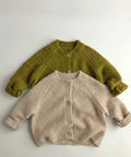 Two knitted cardigans, one green and one beige, on a light gray background.