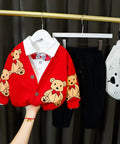 Red cardigan with bear pattern on a hanger against a black curtain background