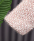 Close-up of a hand wearing a pink textured sleeve with a blurred green leaf in the background