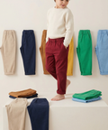 Child standing on a white surface with colorful pants displayed around them.