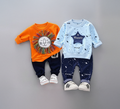 Two children's outfits with orange and navy lion-themed top and blue and navy star-themed top on a gray background.